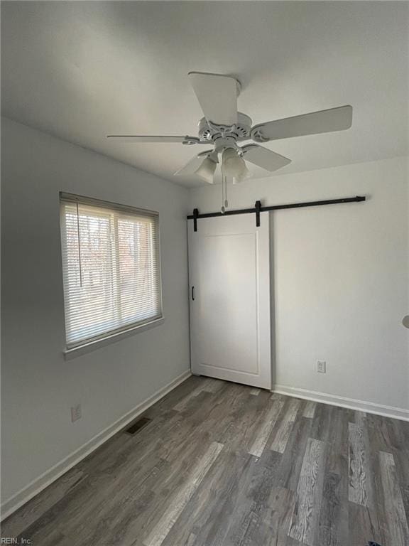 unfurnished bedroom featuring visible vents, a barn door, baseboards, and wood finished floors