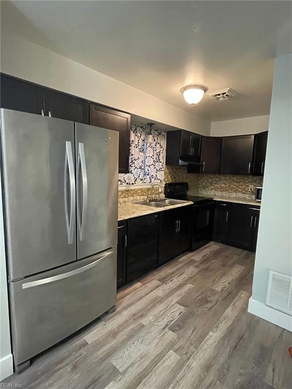 kitchen featuring a sink, light wood finished floors, light countertops, freestanding refrigerator, and black / electric stove