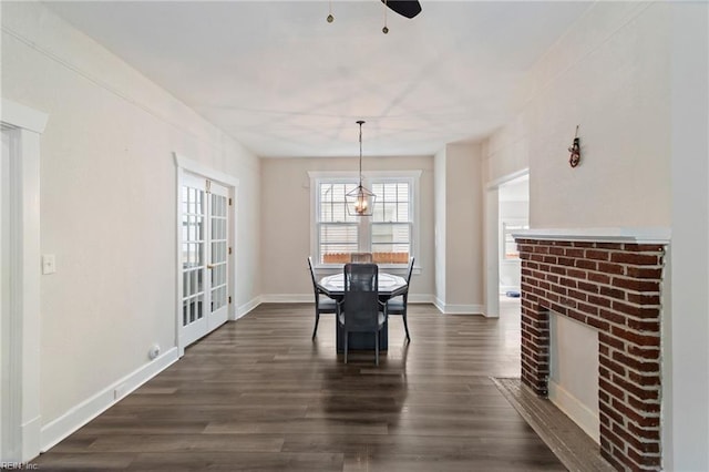 dining room with dark wood finished floors, baseboards, a ceiling fan, and a brick fireplace