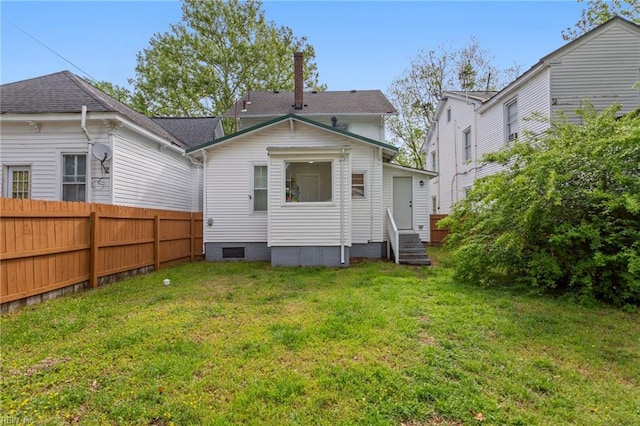 back of house featuring fence, a chimney, a lawn, and entry steps