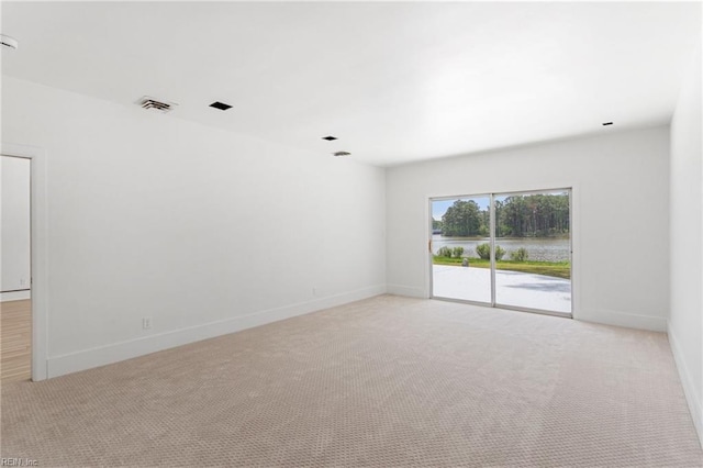 unfurnished room featuring visible vents, baseboards, a water view, and light carpet