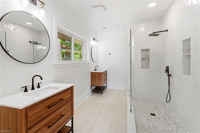 bathroom with a walk in shower, two vanities, baseboards, and a sink