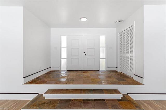 foyer with baseboards, visible vents, and stone tile flooring