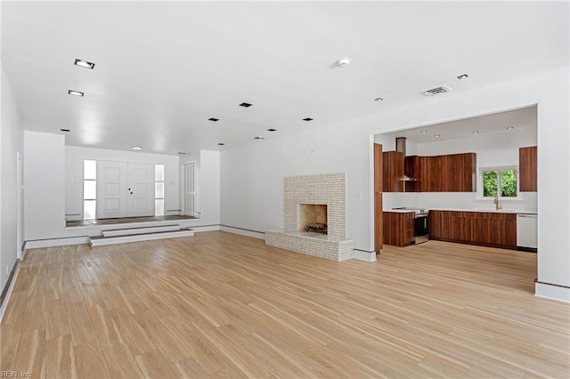 unfurnished living room with a brick fireplace, visible vents, light wood-style flooring, and baseboards