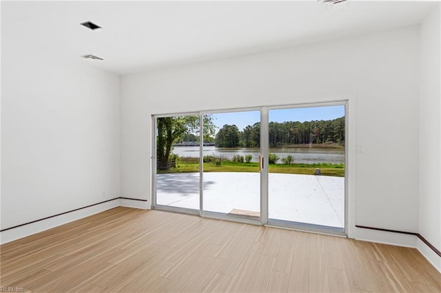 empty room with visible vents, light wood-type flooring, a water view, and baseboards
