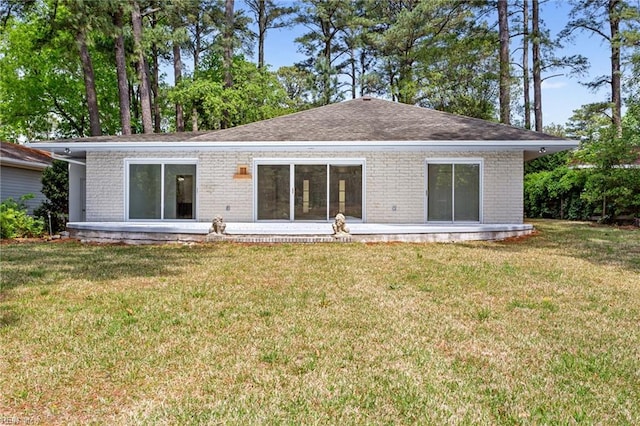 rear view of property with a lawn, roof with shingles, and brick siding