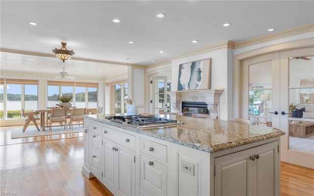kitchen with crown molding, stainless steel gas cooktop, light stone counters, and a wealth of natural light