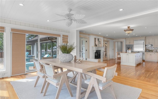 dining space with a fireplace with raised hearth, ceiling fan, recessed lighting, and light wood-style floors