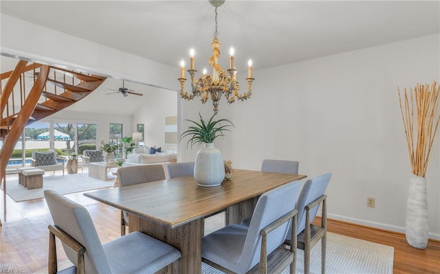 dining room with stairs, light wood-style floors, baseboards, ceiling fan with notable chandelier, and vaulted ceiling