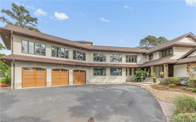 view of front of property featuring an attached garage, driveway, stucco siding, and stone siding