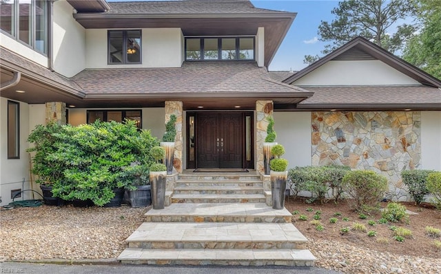 property entrance featuring stone siding, roof with shingles, and stucco siding