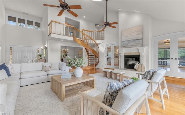 living room featuring a glass covered fireplace, ceiling fan, high vaulted ceiling, stairway, and french doors