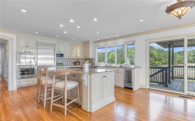 kitchen with ornamental molding, light wood finished floors, wine cooler, and stainless steel appliances