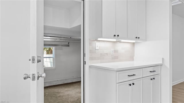 interior space with baseboards, white cabinets, backsplash, and light countertops