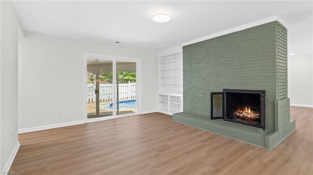 unfurnished living room featuring a fireplace, wood finished floors, baseboards, and built in shelves