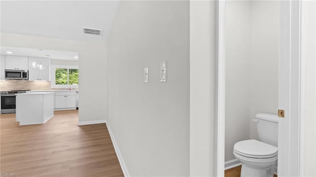 bathroom featuring tasteful backsplash, wood finished floors, toilet, baseboards, and visible vents