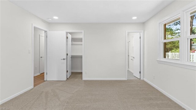 unfurnished bedroom with connected bathroom, a spacious closet, light carpet, and baseboards