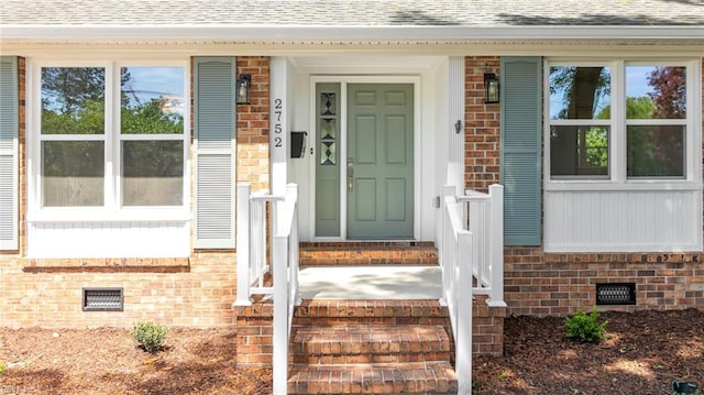 view of exterior entry with brick siding, a shingled roof, and crawl space