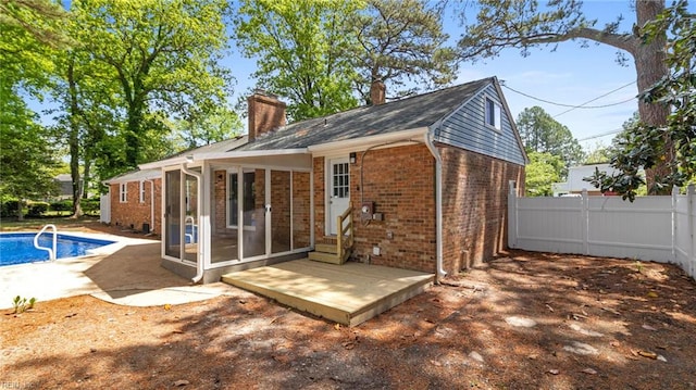 rear view of house featuring fence, a chimney, brick siding, and a sunroom