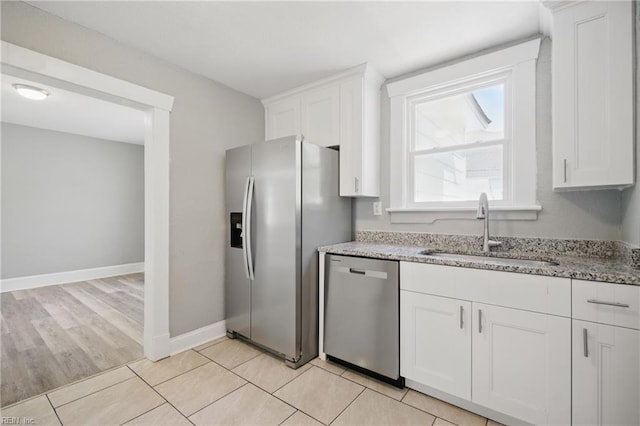 kitchen with light stone counters, appliances with stainless steel finishes, white cabinets, a sink, and baseboards