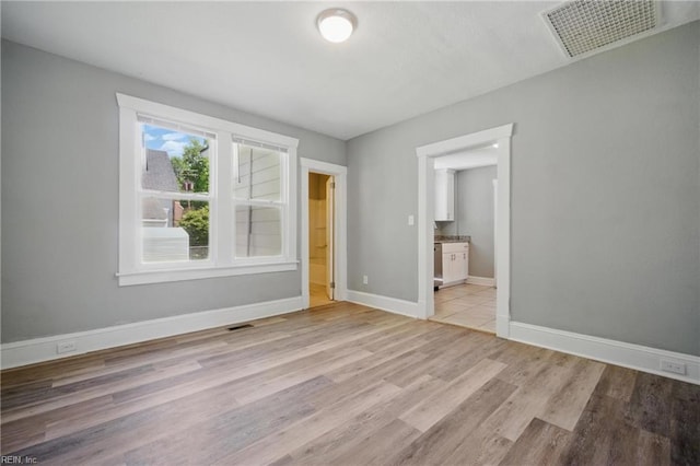 unfurnished bedroom with visible vents, ensuite bathroom, light wood finished floors, and baseboards