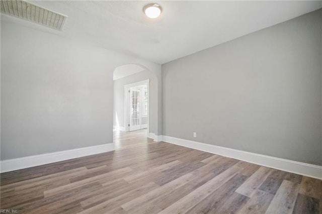 empty room with baseboards, visible vents, arched walkways, and wood finished floors