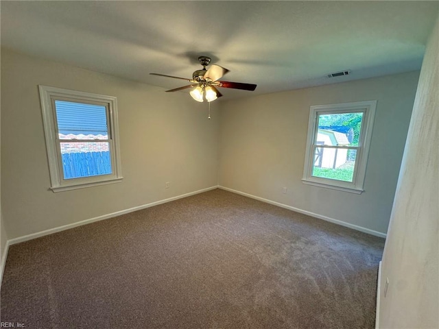 spare room with visible vents, ceiling fan, dark colored carpet, and baseboards