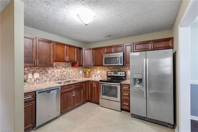 kitchen with light stone countertops, decorative backsplash, stainless steel appliances, a sink, and visible vents