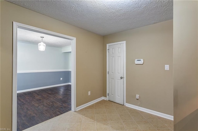 tiled spare room featuring a textured ceiling and baseboards