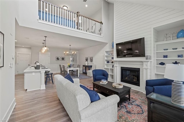 living room with light wood finished floors, a high ceiling, a large fireplace, a chandelier, and baseboards