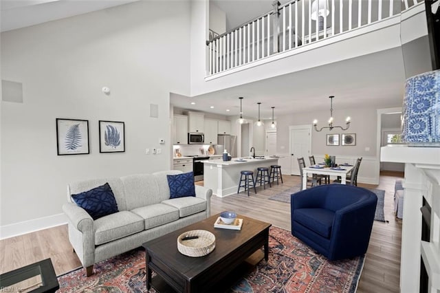 living area with baseboards, a notable chandelier, light wood-style floors, and a towering ceiling