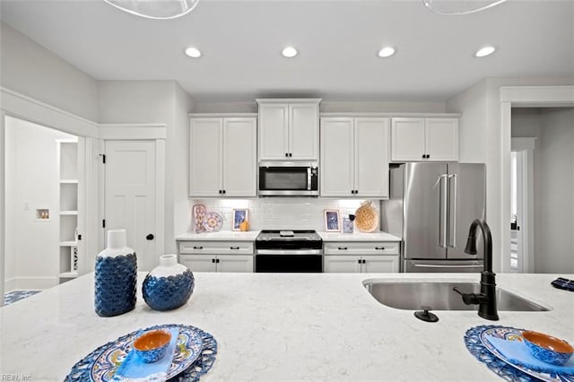 kitchen featuring white cabinets, light stone countertops, appliances with stainless steel finishes, and a sink