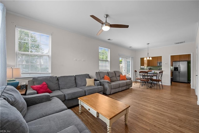living room featuring ornamental molding, a ceiling fan, light wood-style flooring, and visible vents
