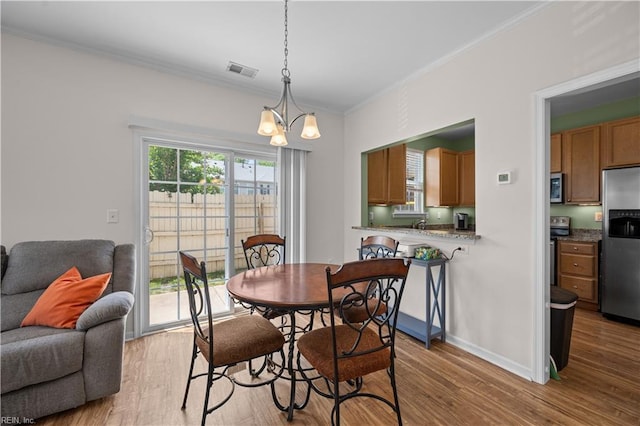 dining area featuring visible vents, ornamental molding, light wood finished floors, and an inviting chandelier
