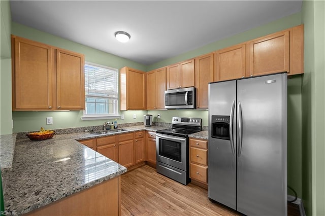 kitchen with appliances with stainless steel finishes, light stone counters, a sink, light wood finished floors, and light brown cabinets