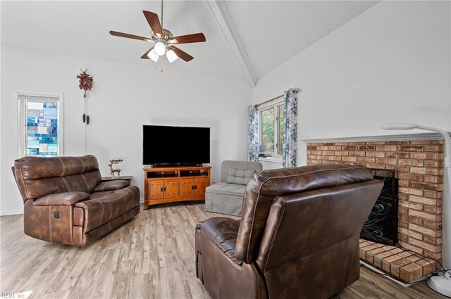 living area featuring lofted ceiling with beams, a ceiling fan, light wood-style flooring, and a brick fireplace