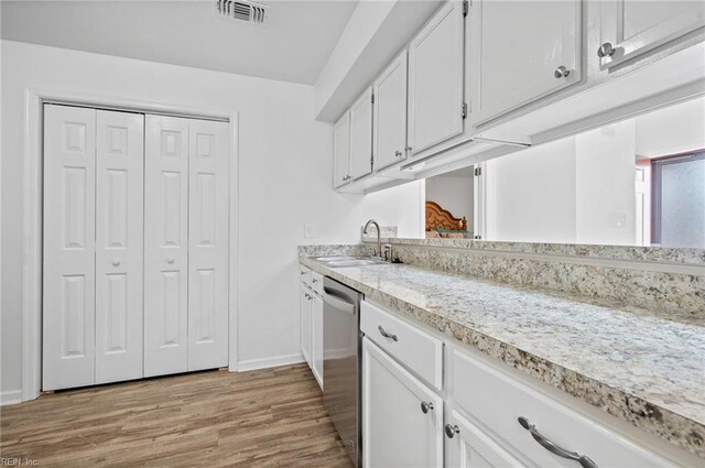 kitchen featuring stainless steel dishwasher, light countertops, white cabinets, a sink, and baseboards