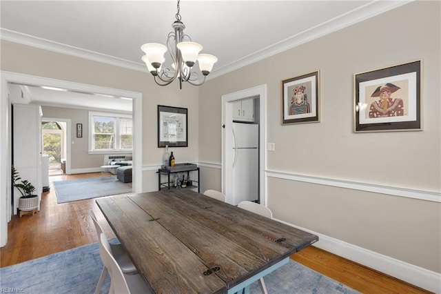 dining space featuring crown molding, an inviting chandelier, wood finished floors, and baseboards