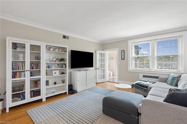 living area with visible vents, ornamental molding, light wood-type flooring, and radiator heating unit