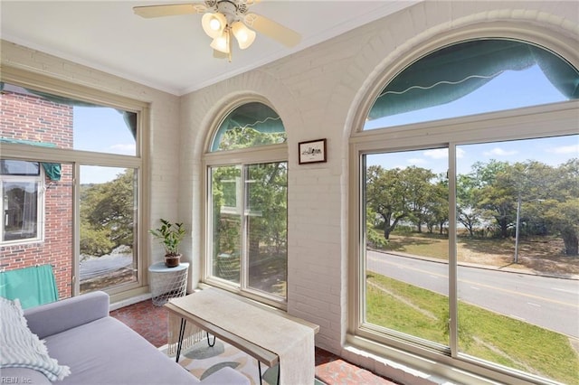 sunroom / solarium featuring ornamental molding, a ceiling fan, and brick wall