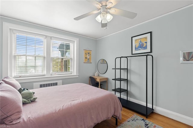 bedroom featuring crown molding, baseboards, radiator heating unit, wood finished floors, and a ceiling fan