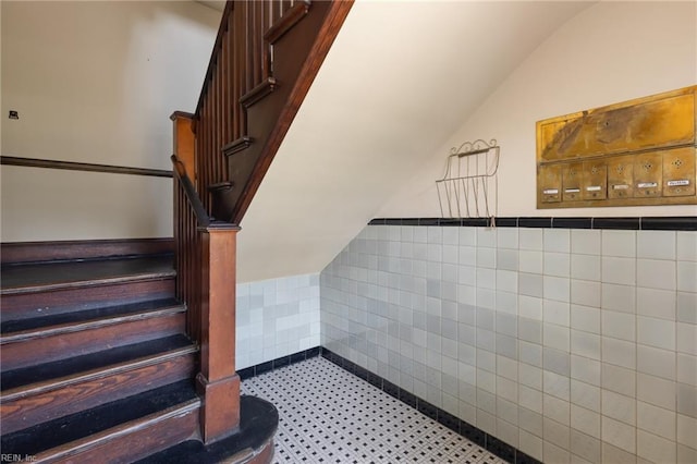 stairway with tile walls, wainscoting, and vaulted ceiling