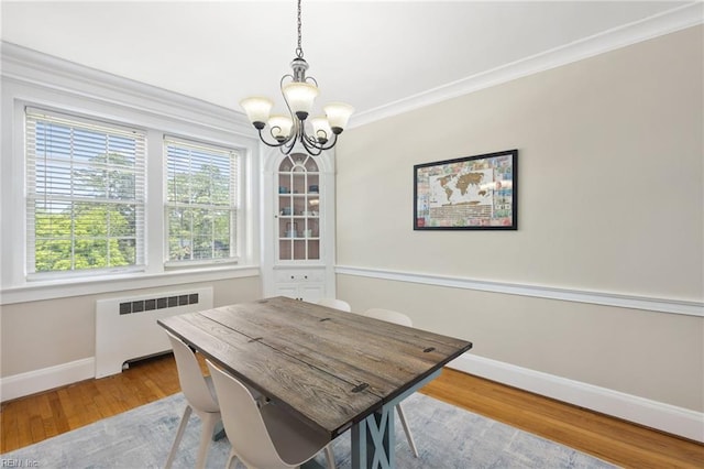 dining area featuring a notable chandelier, crown molding, radiator heating unit, baseboards, and wood finished floors