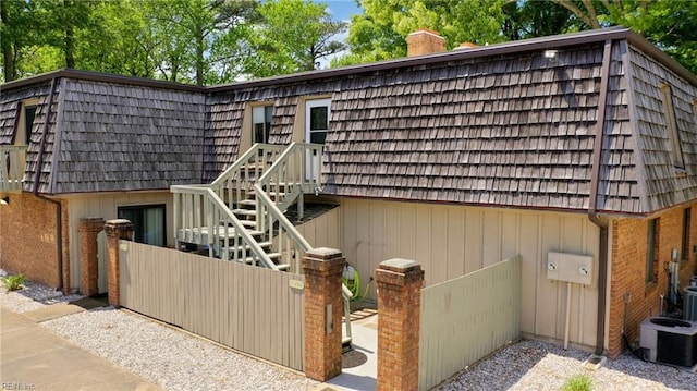exterior space with mansard roof, a chimney, and central AC