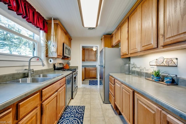 kitchen with brown cabinetry, light tile patterned floors, appliances with stainless steel finishes, and a sink