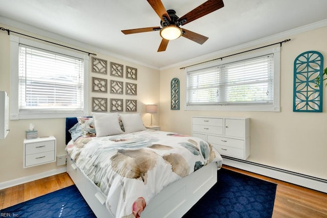 bedroom with wood finished floors, baseboard heating, ornamental molding, baseboards, and a ceiling fan