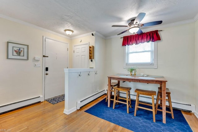 dining room with a ceiling fan, wood finished floors, a baseboard heating unit, and crown molding