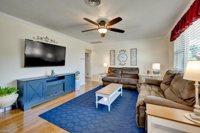 living room with visible vents, a ceiling fan, crown molding, and light wood-style flooring
