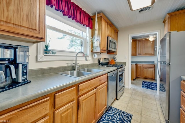 kitchen with appliances with stainless steel finishes, light tile patterned floors, brown cabinets, and a sink