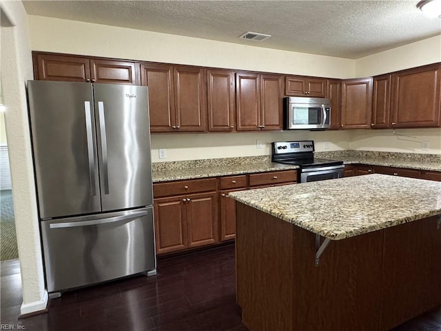kitchen with light stone countertops, appliances with stainless steel finishes, a kitchen island, dark wood-style flooring, and a textured ceiling